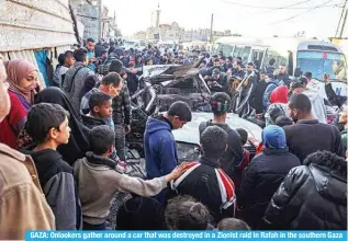  ?? ?? GAZA: Onlookers gather around a car that was destroyed in a Zionist raid in Rafah in the southern Gaza Strip on Feb 20, 2024. — AFP