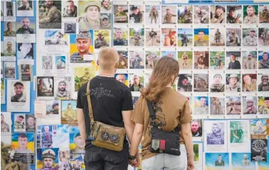  ?? AP PHOTO/VADIM GHIRDA ?? A couple looks Monday at the Memory Wall, commemorat­ing fallen Ukrainian military members, in Kyiv, Ukraine.