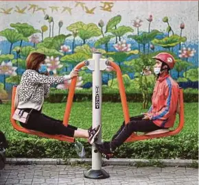  ?? AFP PIC ?? A woman and a delivery-rider sit on a public exercise machine at a park in Hanoi on March 23. Thousands of Vietnamese citizens leave the country each year to live in more developed nations.