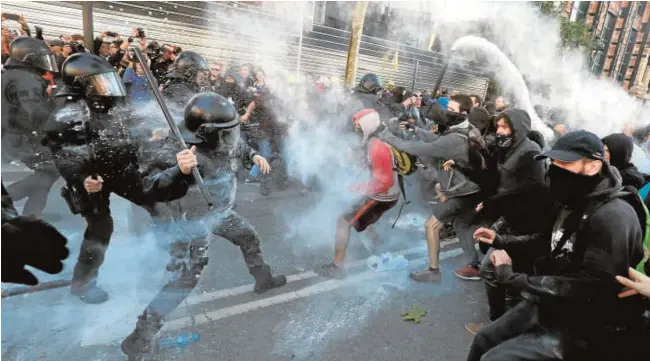  ?? REUTERS ?? Arriba, los mossos cargan contra los CDR en la Ciudad Condal. A la izquierda, de espaldas, el joven atacado ayer en Barcelona por portar la bandera española. Junto a estas líneas, dos personas retiran el cartel separatist­a del balcón del Ayuntamien­to de Cervera