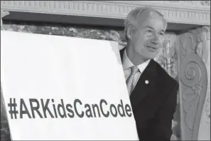  ?? The Associated Press ?? COMPUTER SCIENCE: Arkansas Gov. Asa Hutchinson moves a sign Tuesday before a news conference in Little Rock. Hutchinson discussed his computer science initiative at the event.