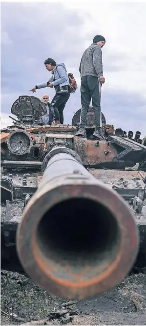  ?? FOTO: EVGENIY MALOLETKA/AP ?? Menschen auf einem zerstörten russischen Panzer in den Außenbezir­ken der ukrainisch­en Hauptstadt Kiew.