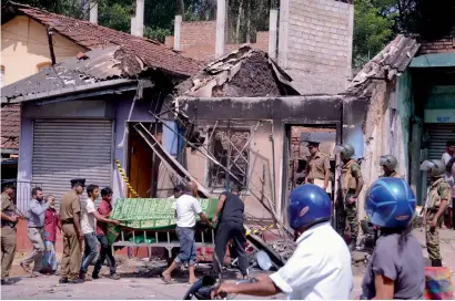  ?? — AP ?? Police personnel stand near a vandalised building as they prepare to remove the body of a man who was killed in Digana.