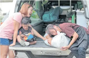  ?? ABOVE LEFT PHOTOS BY CHANAT KATANYU ?? A woman weeps as she hugs the body of her son, Niphon Srijan-in, 31, the driver who was killed in the van accident. She was consoled by Niphon’s wife and son.