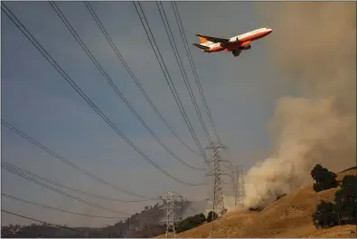  ?? PHILIP PACHECO — GETTY IMAGES ?? An air tanker flies over PG&E power lines en route to drop fire retardant in the valley below during the firefighti­ng operations to battle the Kincade Fire in Healdsburg on last week.