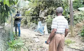  ?? KENYON HEMANS ?? A resident, reportedly the grandfathe­r of one of the victims, looks on as a policeman monitors the cordoned-off crime scene in Hashburn, off Brooks Level Road in Stony Hill.