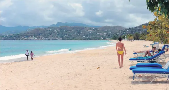  ?? DAVID MCFADDEN/THE ASSOCIATED PRESS FILES ?? Visitors walk on the white sand of the Grand Anse Beach in Grenada, one of the Caribbean island nations that is open for business as usual.