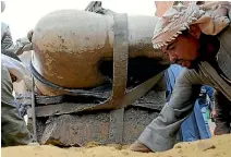  ??  ?? An Egyptian worker prepares the ground as the torso is lowered on to dry land, before being taken away for restoratio­n at a museum.