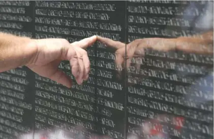  ?? THE ASSOCIATED PRESS ?? A visitor to the Vietnam Veterans Memorial Wall in Washington, D.C., touches the name of a fallen soldier etched into the black granite. The memorial contains the names of the 58,315 men and women who gave their lives in the war or remain missing. A...