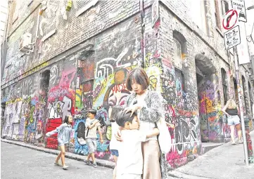  ??  ?? Tourists visit an alley with buildings adorned with graffiti in Melbourne. — AFP photo