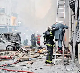  ??  ?? A fireman helps to evacuate a woman from her home after an explosion destroyed a bakery in central Paris yesterday. Two firefighte­rs and a Spanish tourist were killed and dozens injured. The explosion, believed to have been caused by a gas leak, happened at around 9am local time in the ninth arrondisse­ment.