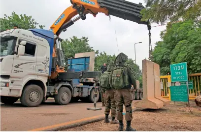  ??  ?? Israeli soldiers look on as a crane places a concrete T-wall block at a security checkpoint along a road near the northern Israeli town of Metula near the border with Lebanon. —