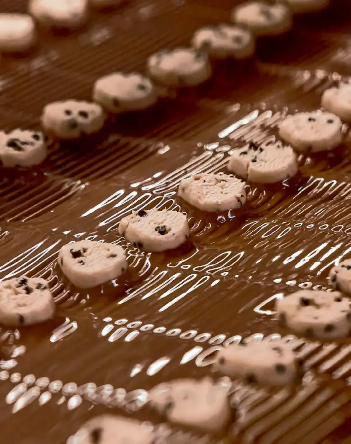  ?? Photos by Jessica Christian/The Chronicle ?? Vanilla chip mixture is coated on the bottom with milk chocolate as it moves down the assembly line at the See’s Candies factory in South San Francisco.