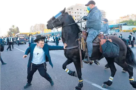  ?? JACKGUEZ/GETTY-AFP ?? Anti-draft protest: A mounted Israeli police officer helps move ultra-Orthodox Jewish protesters blocking a highway Sunday in the central Israeli city of Bnei Brak. Protesters decried the detention of a member of their community who refused to perform compulsory military service. In related news, Israel entered its third coronaviru­s lockdown.
