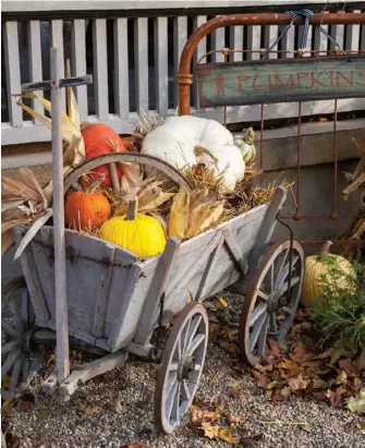  ??  ?? Right: “Seasonal groupings outside add to the quaint and cozy country style that I’ve tried to create,” Cindy shares. For this charming vignette, she filled a primitive European goat wagon with colorful pumpkins, corn and gourds and then popped an antique wagon wheel into the middle. As a backdrop, Cindy propped up an old metal headboard that serves as a sign holder.