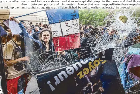  ??  ?? A protester holds a French tricolored flag with an anti-Macron slogan outside a destroyed McDonald’s fast food restaurant during a rally to mark the annual May Day marches in Paris on Tuesday.