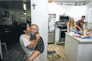  ?? ?? ABOVE: Sol, left, a 14-year-old from Argentina, kisses 8-year-old foster sister Maddie Hazelton as they play together last week in the kitchen of Sol’s foster parents, Andy, right, and Caroline Hazelton, in Homestead, Fla. The Hazeltons also have housed migrant minors from Afghanista­n and Central America.
