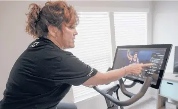  ?? KEITH SRAKOCIC/AP ?? Cindy Cicchinell­i points out others on the screen listed to be cycling at the same time as she watches the online video while using her Peloton exercise machine at her Pittsburgh townhouse.