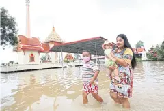  ?? ?? IN SEARCH OF A BIT OF DRY: A family walks in the floodwater at Wat Sakae in Sam Khok district, Pathum Thani. The water in the Chao Phraya River has risen, flooding the temple ground.