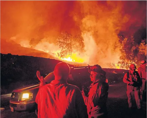  ??  ?? WALL OF HEAT: Firefighte­rs confer while battling the fire near Geyservill­e in northern California’s wine-growing Sonoma County