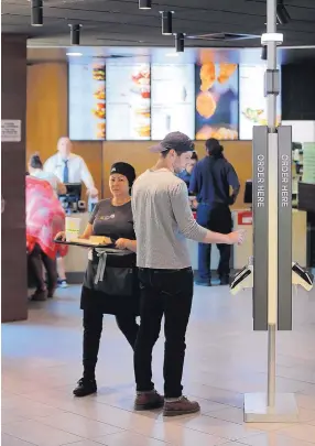  ??  ?? Michael Quigley, right, orders food at a self-service kiosk, while Leni Bortolato delivers a meal for a dining-room guest at a McDonald’s restaurant in Chicago. The company that helped define fast food is making supersized efforts to reverse its fading...