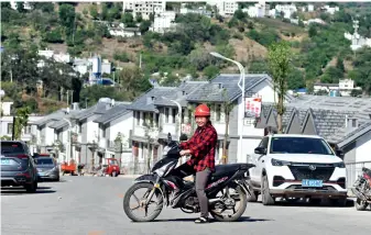  ??  ?? Tous les jours, Xu Guocong se rend au travail à moto. Derrière elle, le nouveau village construit pour les paysans migrants.