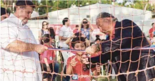  ??  ?? Jorge Rolando Bauger, derecha y Jorge Allen Bauger, ayudan a uno de los niños a cortar la cinta que deja oficialmen­te abiertas las nuevas facilidade­s de la escuela de fútbol Jorge Rolando Bauger.