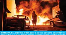  ?? — AFP ?? MINNEAPOLI­S: A man tries to tow away a car in a safe zone as another car catches fire in a local parking garage on Friday during a protest over the death of an unarmed black man.