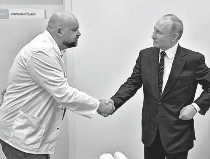  ?? ALEXEI DRUZHININ/SPUTNIK ?? Russian President Vladimir Putin, right, shakes hands with hospital chief Denis Protsenko while visiting COVID-19 patients in March in Kommunarka, Russia.