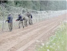  ?? ?? Polish soldiers build a fence on the border between Poland and Belarus. Thousands of migrants have crossed or tried to cross into the European Union from Belarus in recent months. — Reuters