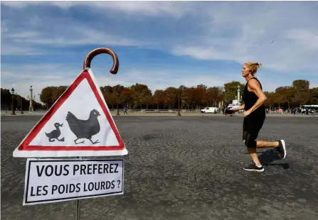  ??  ?? No wheels, no problem: A woman jogging past a sign reading “Do you prefer heavy trucks?” during a vehicle-free day in Paris. — AFP