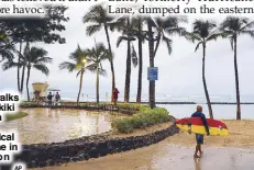  ??  ?? A surfer walks along Waikiki Beach in a light rain from Tropical Storm Lane in Honolulu on Saturday. AP