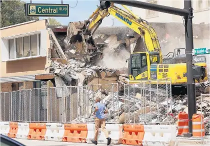  ?? STEPHEN M. DOWELL/ORLANDO SENTINEL ?? A pedestrian jogs swiftly by as a 7-Eleven store is demolished at the corner of North Rosalind Avenue and Central Boulevard in Orlando on Monday. The demolition of the structure is to allow for the expansion of the City of Orlando’s signature Lake Eola Park.