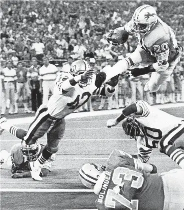  ?? [AP PHOTO] ?? Billy Sims leaps past the San Francisco 49ers’ Ronnie Lott (42) and Terry Tautole (50) into the end zone for the winning touchdown in a 1981 game between the Detroit Lions and the 49ers at the Pontiac Silverdome.