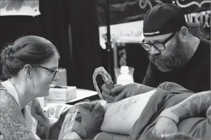  ?? Herald photo by Greg Bobinec ?? Monty and Lesile Rickens from Monsters Ink Tattoo in Medicine Hat double-team a piece at the Windy City Tattoo Convention at Exhibition Park, Saturday afternoon.