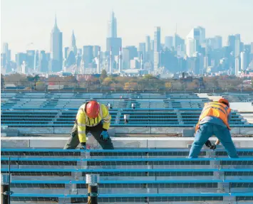  ?? MARY ALTAFFER/AP 2021 ?? With the Manhattan skyline in the distance, electricia­ns install solar panels atop a terminal garage at LaGuardia Airport in the New York borough of Queens.