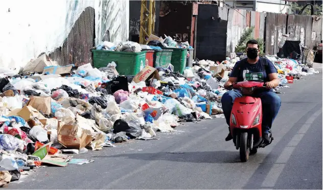  ?? Reuters ?? ↑
A man rides a motorbike past piled-up garbage along a street in Ain Al Remmaneh on Monday.