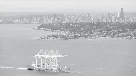  ?? TED S. WARREN, THE ASSOCIATED PRESS ?? With the Seattle skyline as a backdrop, a ship carrying four of the West Coast’s largest container cranes passes through Puget Sound on Friday. The cranes, which will be installed at the Husky Terminal at the Port of Tacoma, will give the port the...