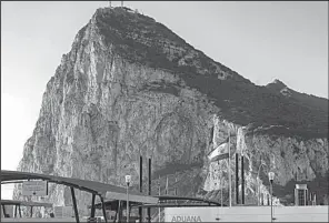  ?? AP/DANIEL OCHOA DE OLZA ?? The Rock of Gibraltar towers over the U.K. enclave as a Spanish flag flies atop the customs house on Spain’s side of the border. Spain ceded Gibraltar to Britain in 1713.