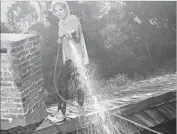  ?? Ellis R. Bosworth Associated Press ?? ACTRESS Kim Novak uses a garden hose to wet the roof of her Bel-Air mansion during the 1961 fire.