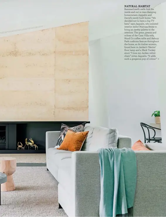 ??  ?? NATURAL HABITAT Rammed-earth walls link the inside and out in tree-changing homeowners Jappalin and
David’s newly built home. “We decided not to have a big TV here,” says Jappalin, who enlisted interior stylist Malvina Stone to bring an earthy palette to the interiors. The greys, greens and ochres of the Casa Villa sofa, Nood Co coffee table and Asbury Park cushions feature throughout the home, as do timber accents, found here in Jardan’s ‘Hector’ floor lamp and a Mark Tuckey stool. “I love my Jardan velvet chair,” notes Jappalin. “It adds such a gorgeous pop of colour.” >