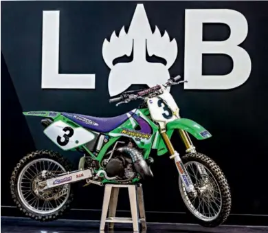  ??  ?? Le logo du LAB derrière la moto d’emig, c’est un anachronis­me ! Création récente, ce laboratoir­e invente les tenues du futur. La tenue limitée Blue Label de Roczen y a été développée en secret.