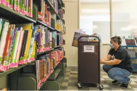  ?? Nick Otto / Special to The Chronicle ?? Cristina Flores, a library aide, works in Oakland Public Library’s acquisitio­ns department. When libraries reopen, patrons’ access to materials will change.