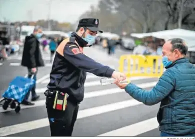  ?? FERNANDO VILLAR / EFE ?? Un agente ofrece gel hidroalcoh­ólico a un hombre a su llegada ayer a un mercadillo de Alcalá de Henares (Madrid).