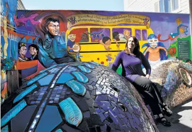  ?? Michael Macor / The Chronicle ?? Author Cary Cordova sits on Mark Roller’s 1982 sculpture “The Gifts of Quetzalcoa­tl” while checking out Tirso Gonzalez Araiza’s 2015 mural “The Resistance Game” at the mini park at 24th and York streets.