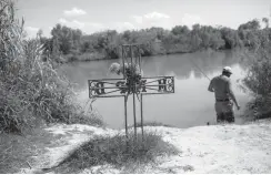  ?? Associated Press ?? n A man fishes in the river on March 25 near a cross erected in memory of a migrant who died trying to cross to the U.S. The cross stands on the bank of the Rio Grande river in Nuevo Laredo, Tamaulipas state, Mexico, across the border from Laredo, Texas.