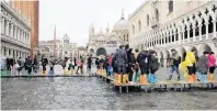  ??  ?? People walk on a catwalk in a flooded Saint Mark Square, in Venice.