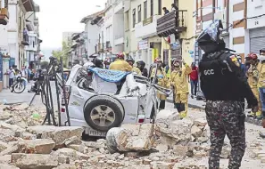  ?? AP ?? A police officer looks up next to a car crushed by debris after an earthquake shook Cuenca, Ecuador on Saturday.