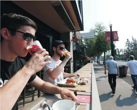  ?? PHOTOS: JIM WELLS ?? Hayden Cameron, left, and Owen Goerzen enjoy a prime spot and a cold beverage at Trolley 5 during the lunch hour on Friday.