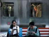  ?? ANDY WONG — THE ASSOCIATED PRESS ?? Shoppers sit on a bench decorated with a U.S. flag while browsing on their smartphone­s Monday outside a fashion boutique selling U.S. brand clothing in Beijing.